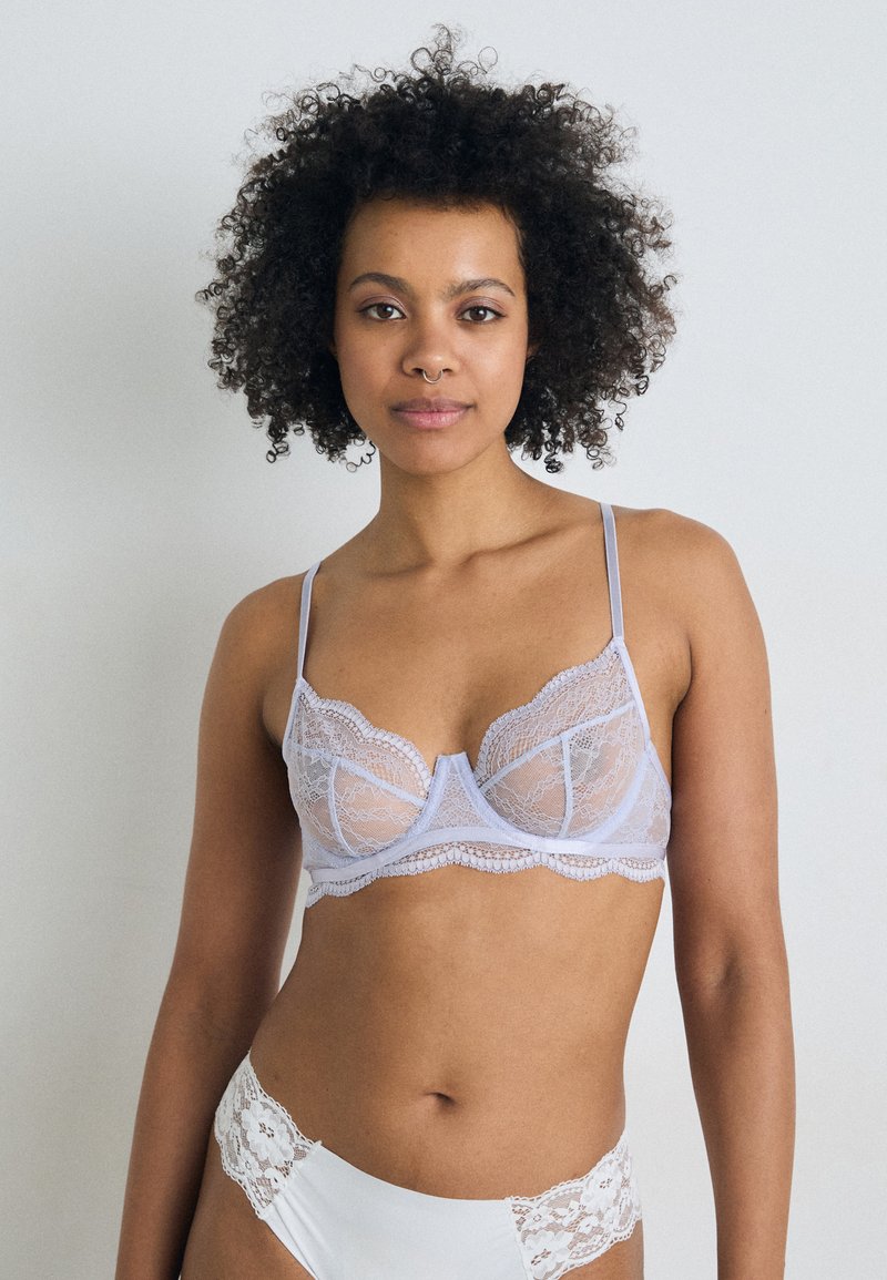 Kanten bralette in licht lavendel met ingewikkelde geschulpte randen, semi-transparante cups en dunne verstelbare bandjes. Inclusief een bijpassende witte kanten slip.