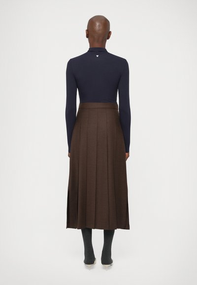 Marineblå langærmet top parret med en plisseret brun nederdel. Outfittet har en talje og høje slidser i kanten, blød tekstur.