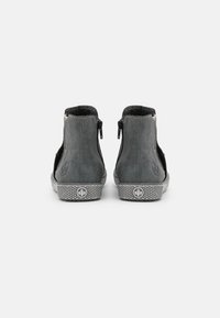 Bottes montantes grises avec une texture semblable à du daim, présentant des panneaux latéraux noirs, des coutures nettes et des fermetures éclair à l'arrière. Semelle en caoutchouc avec un motif.