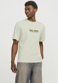 Lyscreme bomulds T-shirt med korte �ærmer, der har en grøn tekstdesign "THRILL CINEMA HORROR FILMS ONLY" på forsiden. Velegnet til afslappet brug.