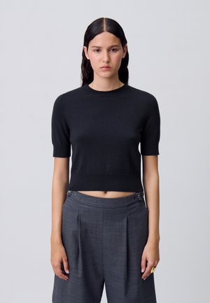 Top corto in maglia nera con maniche corte. Materiale morbido, collo e orlo a coste. Abbinato a pantaloni grigi plissettati con bottoni argentati.