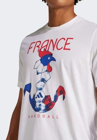 Vit bomull t-shirt med en grafisk design av en tupp i rött och blått med texten "FRANKRIKE" och "HANDBOLL", korta ärmar, rundad halsringning.