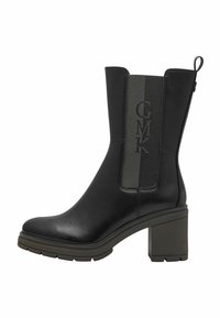 Bottine en cuir noir avec un talon carré, dotée d'un panneau en tissu vert texturé et d'une marque en relief sur le côté.