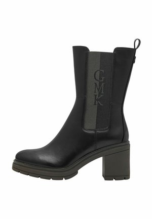 Bottine en cuir noir avec un talon carré, dotée d'un panneau en tissu vert texturé et d'une marque en relief sur le côté.