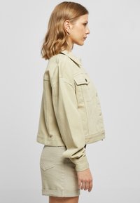 Chaqueta de denim beige con un corte cropped, mangas oversized y bolsillos frontales. Combinada con una falda corta beige a juego.