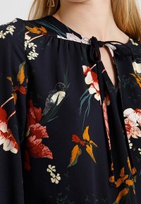 Bloemige blouse van donker marineblauwe stof met levendige, multicolore bloemen. Inclusief een striksluiting bij de halslijn en een zachte, vloeiende textuur.