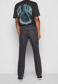 Schwarzes Grafik-T-Shirt mit dem Schriftzug "LEE JEANS" in Türkis, kombiniert mit dunkler Denim-Jeans. Auf der Rückseite schlicht mit zwei Gesäßtaschen.