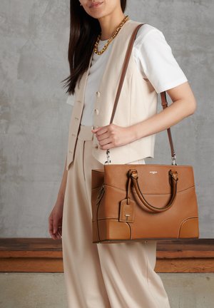Sac à main en cuir marron à texture granuleuse, avec poignées doubles, une bandoulière détachable et une étiquette. Présente des accents cousus et une forme structurée.
