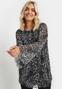 Genomskinlig blus med svart och grå leopardmönster, långa volangärmar och en lös passform. Mjuk textur, avslappnad design med vågig fåll.