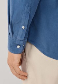 Manica di camicia in corduroy blu con polsini a bottone e patta della manica a punta. Tessuto liscio con sottili righe verticali.