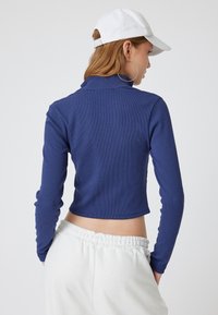 Donkerblauw geribbeld crop top met lange mouwen en een kleine kraag, gecombineerd met witte sweatpants met elastische taille. Soepele textuur.