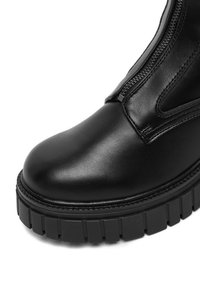 Černé kožené kotníkové boty s kulatou špičkou, bočním zipem a tlustou drsnou podrážkou pro lepší přilnavost. Hladký povrch a minimální detaily.