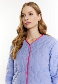 Lyseblå, quilted jakke med bølget mønster, pink kant og matchende knapper. Har lange ærmer og en blød tekstur.