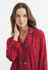 Camisón rojo con acentos verdes, que presenta una variedad de patrones navideños, incluidos camiones y árboles. Tejido suave y liso.