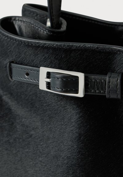 Sac à main en cuir noir texturé avec une boucle rectangulaire argentée sur une sangle près du bord supérieur du sac.