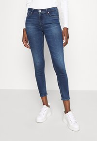 Mörkblå skinnyjeans med hög midja, med framlommer, dragkedja och en slät denimtextur. Matchas med vita sneakers.