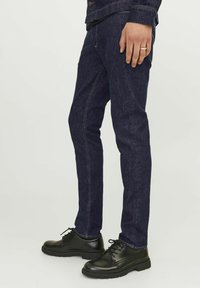 Jeans de mezclilla azul oscuro con un corte ajustado. Combinados con zapatos de cuero negro con punteras redondeadas y suelas texturizadas.