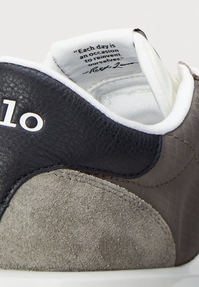 Αθλητικό παπούτσι με μαύρο δέρμα και γκρι σουέτ άνω μέρος, στρογγυλή μύτη, επενδυμένο κολάρο �και λευκό εσωτερικό με εκτυπωμένο απόσπασμα στη γλώσσα.