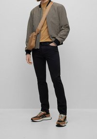 Chaqueta bomber a cuadros, camisa mostaza, vaqueros negros y zapatillas marrones. Pequeño bolso cruzado marrón. Tejido texturizado y colores contrastantes.