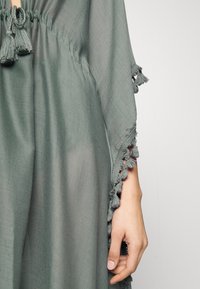 Abito in tessuto leggero di colore verde, con scollo arricciato, dettagli con tasselli sulle maniche e finitura testurizzata.
