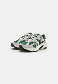 Nike sportcipő zöld és fehér hálós felsőrésszel, szürke velúr díszítésekkel, fekete logóval és textúrált gumitalppal. Zsinórra fűzhető kialakítással rendelkezik.