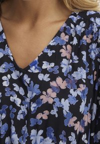 Látka s květinovým vzorem na černém pozadí, obsahující modré a broskvové květy. V-kroj s jemnou texturou a mírným splýváním.