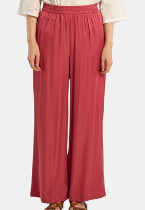 Pantalon ample à jambes larges en tissu doux rougeâtre avec taille élastique, porté avec un chemisier blanc et des sandales marron.