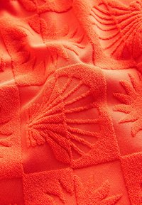 Tissu orange texturé présentant des motifs en relief de coquillages et de formes abstraites, créant une surface tactile et décorée.