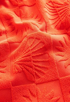 Tissu orange texturé présentant des motifs en relief de coquillages et de formes abstraites, créant une surface tactile et décorée.