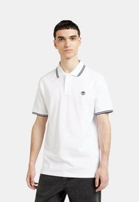 Polo bianco con strisce navy a contrasto sul colletto e sulle maniche, dotato di un piccolo logo ricamato sul petto.