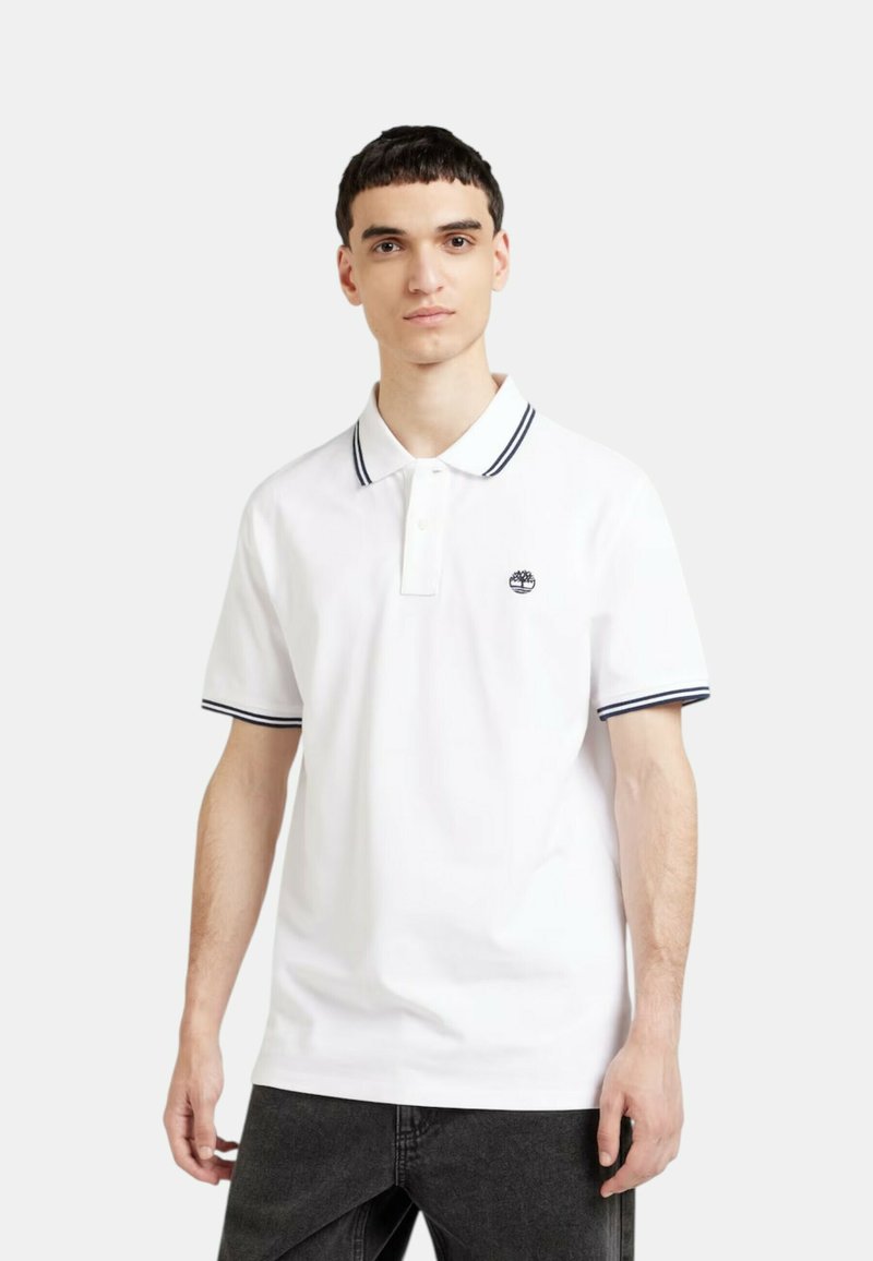Polo bianco con strisce navy a contrasto sul colletto e sulle maniche, dotato di un piccolo logo ricamato sul petto.