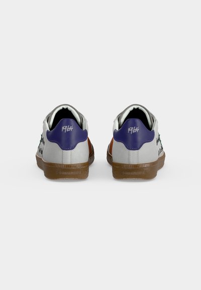 Paire de baskets blanches avec languettes violettes au talon et semelles marron, vues de dos sur un fond clair et uni.