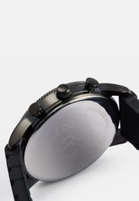 Melnā nerūsējošā tērauda hronogrāfs ar teksturētu rāmīti un trim pogām. Iekļauj melnu gumijas siksnu un pulētu sudraba apakšdaļu.