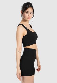 Sujetador deportivo negro con tirantes anchos y un diseño ajustado, combinado con pantalones cortos negros de cintura alta, mostrando una tela suave y sin patrones visibles.