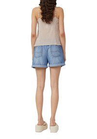 Gestreept beige en witte tanktop, spijkerblauwe shorts met omgeslagen cuffs, en crèmekleurige platform sandalen. Toont de achterkant van de outfit.