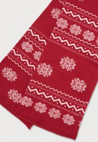 Tecido de malha vermelho com padrões de floco de neve branco e ziguezague, dobrado com textura visível e costura detalhada.