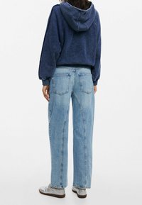 Felpa cropped blu navy con cappuccio regolabile, abbinata a jeans a gamba larga azzurri con tasche posteriori e una texture sbiadita.