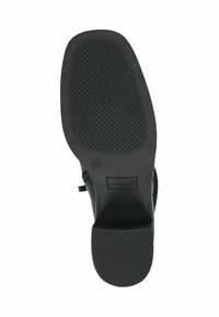 Suela de zapato negra con un agarre texturizado y estampado, que presenta un tacón suave y redondeado, y el logotipo de la marca "Caprice" en relieve.