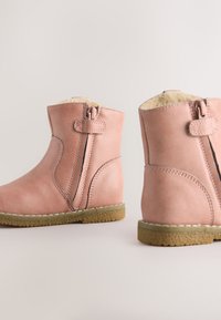 Bottes-chelsea en cuir rose avec une fermeture éclair latérale, une doublure intérieure douce et une semelle en caoutchouc texturée, arborant des détails de couture et des bouts arrondis.