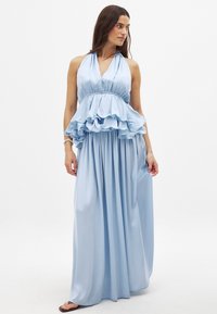 Abito halter azzurro chiaro con un corpetto a peplo arricciato, gonna maxi fluida e texture in satin morbido. Presenta una vita aderente e una silhouette morbida.