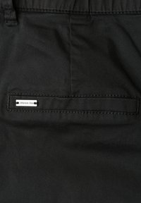 Tissu noir avec une poche arrière horizontale dotée d'une petite étiquette argentée rectangulaire portant l'inscription "Street One."