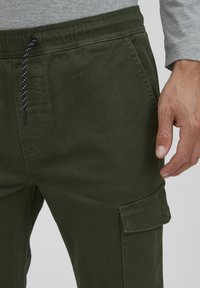 Groene cargobroek gemaakt van katoenmix. Voorzien van een elastische tailleband met trekkoord, zijzakken en een patchzak op het been.