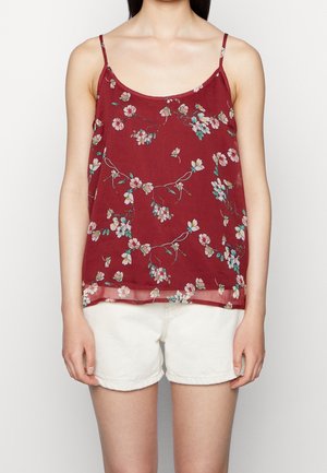 Top in fiorato bordeaux con spalline sottili, caratterizzato da un delicato motivo di fiori rosa e blu su un tessuto trasparente. Abbinato a pantaloni corti bianchi.