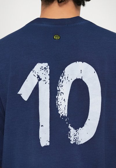 Mørkeblå bomull T-skjorte med et stort hvitt, slitt "10" på ryggen, og en liten grønn logotag ved halsen.
