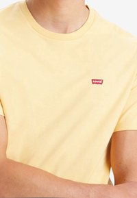 Żółta bawełniana koszulka z okrągłym dekoltem i krótkimi rękawami. Posiada małe czerwone logo Levi's na lewej piersi. Gładka tekstura.