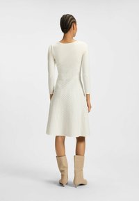 Cream dress with long sleeves and a flared silhouette, featuring subtle dot patterns. Paired with beige knee-high boots.