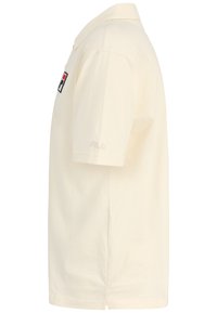 Camiseta polo color crema hecha de algodón, con mangas cortas, un cuello y un logo de Fila bordado en el pecho.