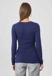 Μπλούζα μακριάς μανικιού σε ναυτική μπλε απόχρωση με εφαρμοστή σχεδίαση, μαλακή υφή και κεντητό λουλούδι γύρω από την λαιμόκοψη. Συνδυάζεται με ανοιχτό γκρι τζιν.