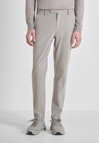 Svijetlosmeđi slim-fit hlače u kombinaciji sa svijetlosmeđim tenisicama, nosene s dugim svijetlosmeđim topom, prikazane od struka do stopala.