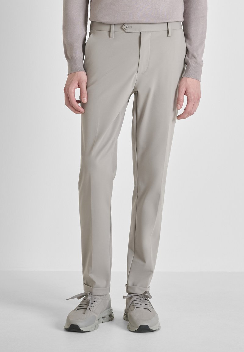 Svijetlosmeđi slim-fit hlače u kombinaciji sa svijetlosmeđim tenisicama, nosene s dugim svijetlosmeđim topom, prikazane od struka do stopala.
